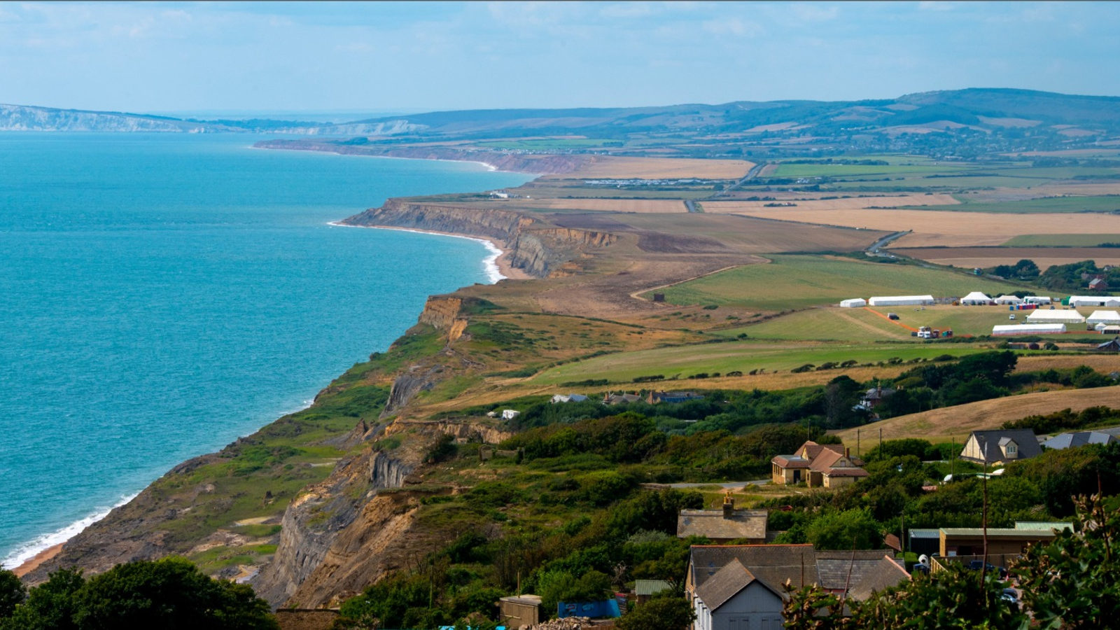 A green coastline of cliffs and fields meeting a turquoise sea under a summer sky