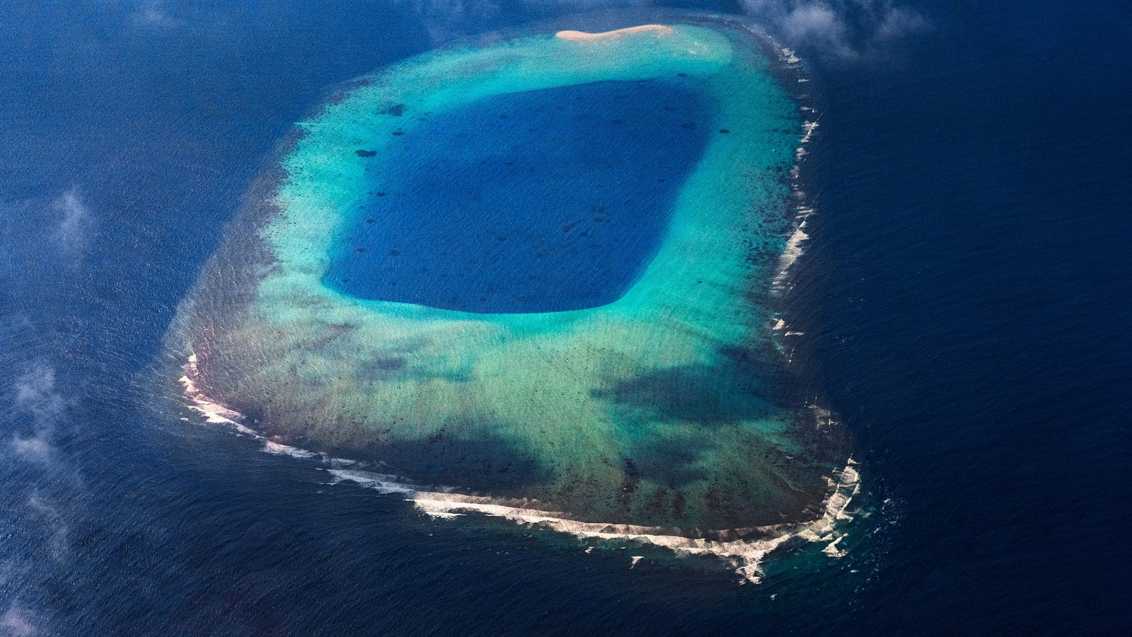 Aerial view of a ring-shaped coral atoll enclosing a turquoise lagoon in the open ocean