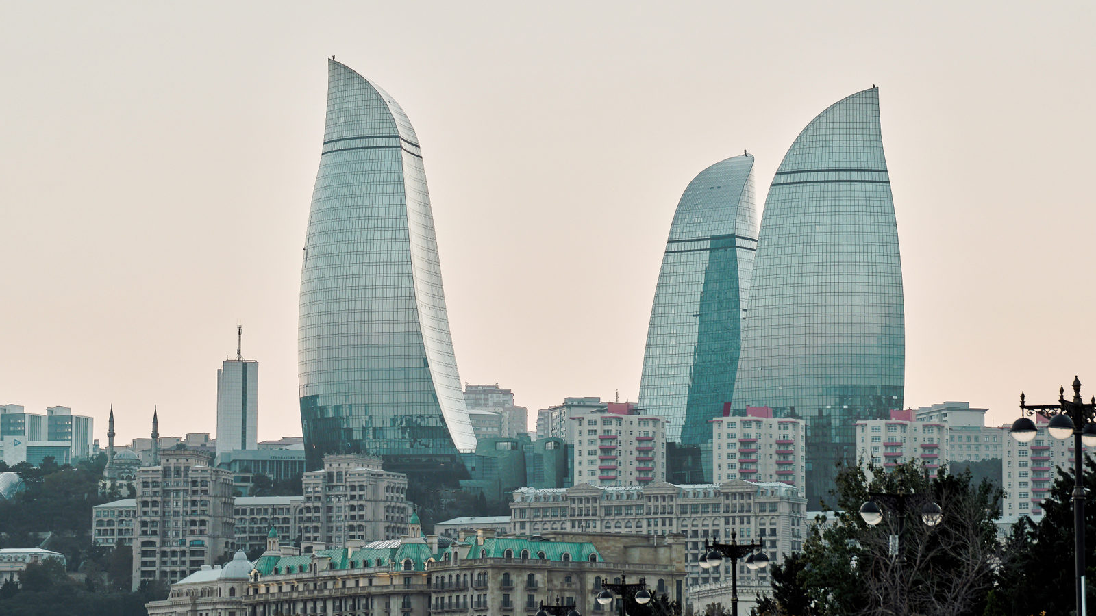 Baku's three sail-shaped Flame Towers rising above the city's older low-rise buildings under a pale sky