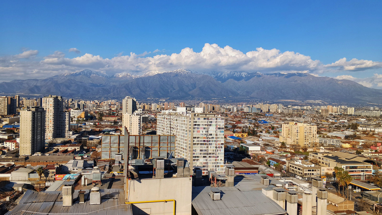 Aerial view of Santiago, Chile's dense cityscape with the snow-capped Andes mountains rising behind it under a bright blue sky
