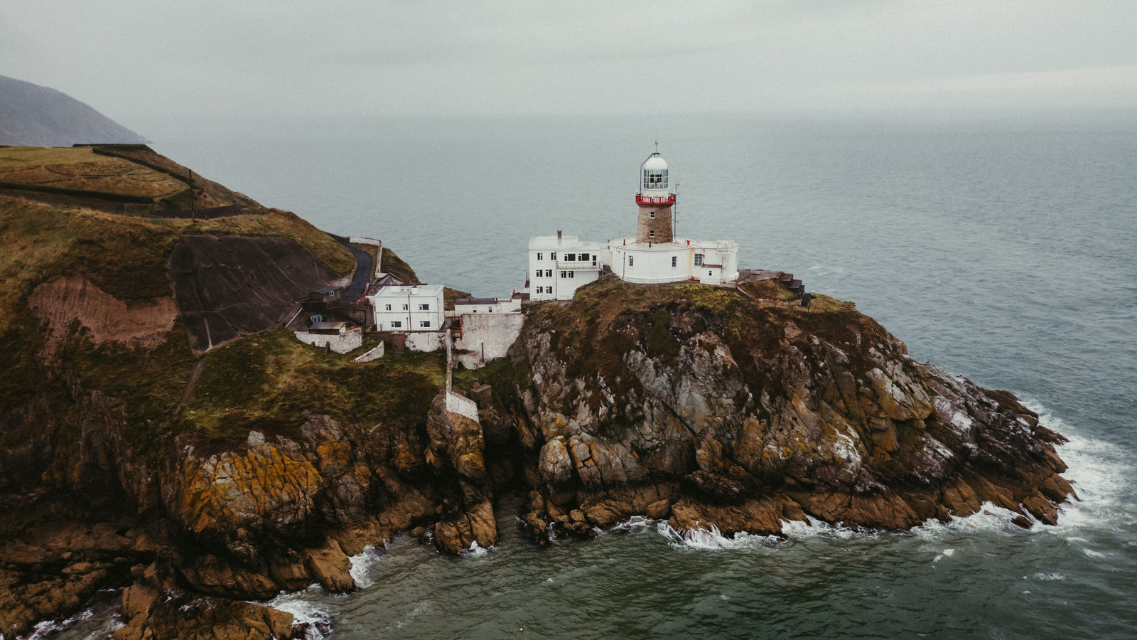 A lighthouse station on a rugged rocky headland jutting into the sea, with waves breaking below the cliffs